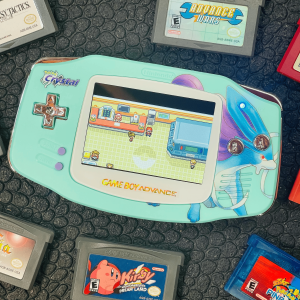 a modded gameboy advance in a light blue shell with a white holographic glass lens. Pokemon Emerald is playing on the screen.